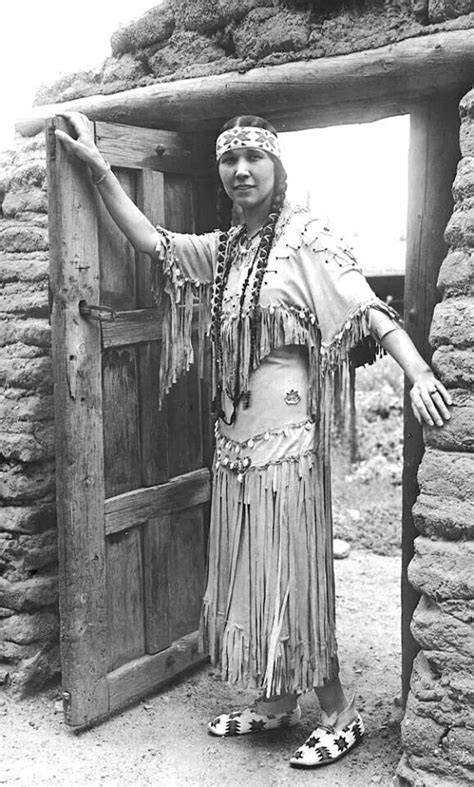 An Old Photo Of A Native American Woman Standing In Front Of A Door