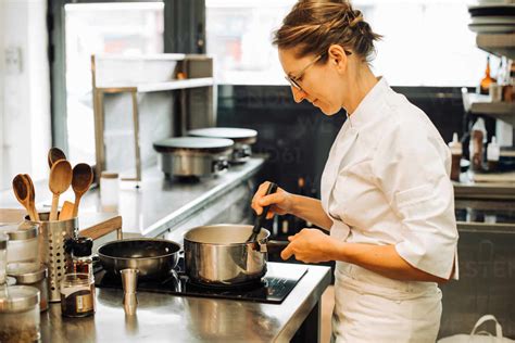 Female Chef Working In Restaurant Kitchen Stirring Hot Food In Pan