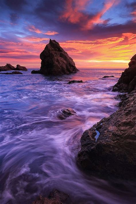 The Sun Is Setting Over The Ocean With Rocks In The Foreground And