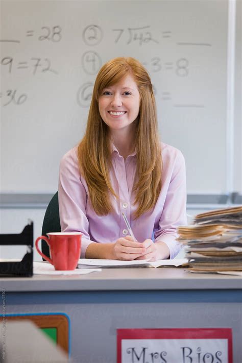 portrait of smiling teacher sitting at desk in classroom by stocksy contributor andersen ross