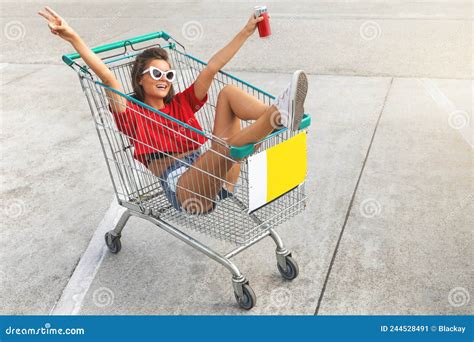 Woman Sitting Inside A Shopping Cart With Soft Drink On The Parking Of Supermarket Stock Image