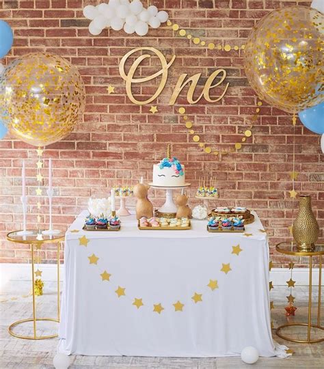 A Table Topped With Cake And Balloons Next To A Brick Wall Covered In Confetti