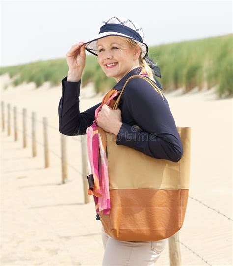 Older Woman Smiling And Holding Her Hat At The Beach Stock Photo