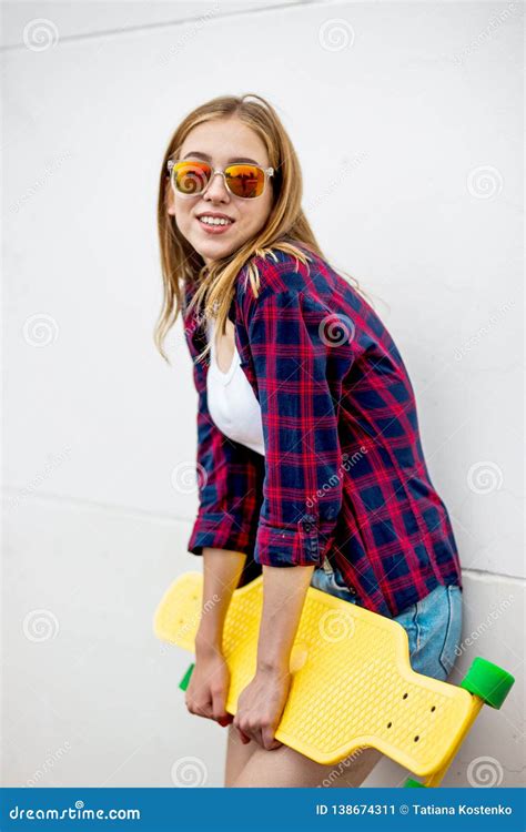 a pretty smiling blond girl wearing sunglasses checkered shirt and denim shorts is standing in