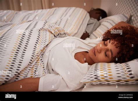 millennial african american woman lying on her back asleep in bed her partner in the background