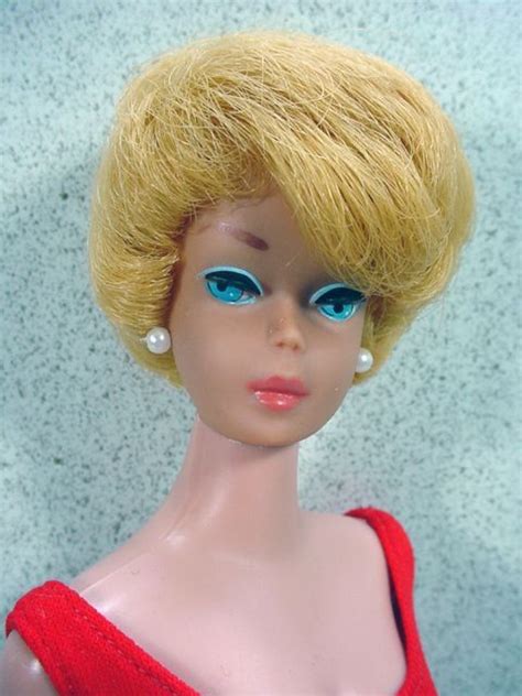 A Doll With Blonde Hair And Blue Eyes Wearing A Red Dress On A White
