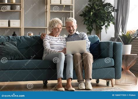 Elderly Couple Resting On Couch Using Laptop Watching Movie Stock Image