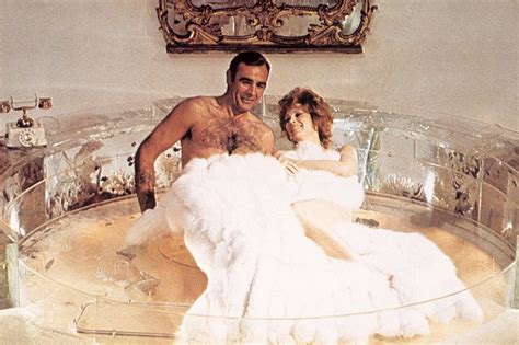 A Man And Woman Sitting In A Bathtub With Fur On The Floor Next To Each