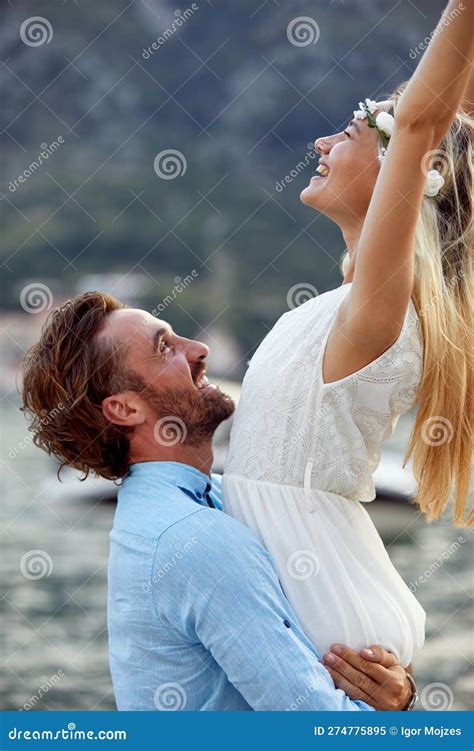 Cheerful Newlywed Couple On Honeymoon Groom Holding Bride In His Arms She Has Her Arms In The