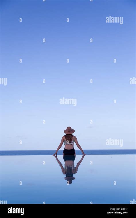 Rear View Of Woman Sitting On The Edge Of An Infinity Swimming Pool
