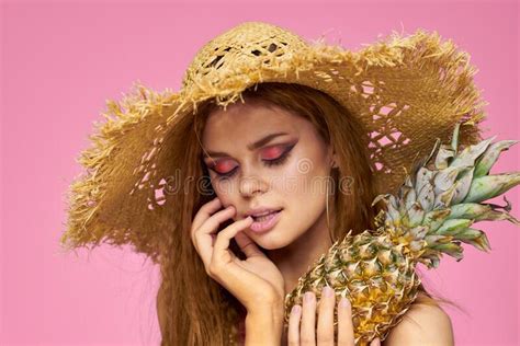 woman with a gun in hands of a straw hat bright makeup exotic fruits summer pink background