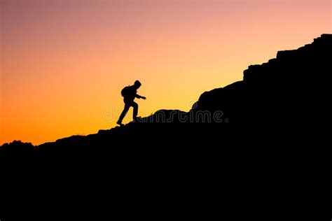 The Silhouette Of A Man Climbing A Mountain In The Sunset Light Stock