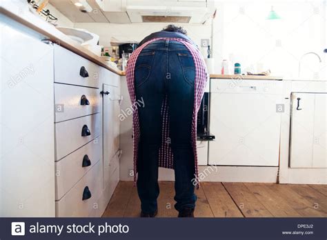 Rear View Of Mature Woman In Kitchen Bending Over Oven Stock Photo