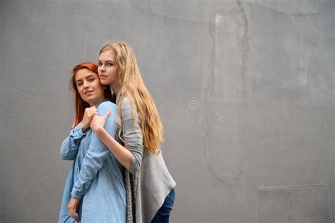 Two Happy Girlfriends Are Hugging On The Background Of A Gray Wall Gentle Hugs Of A Female