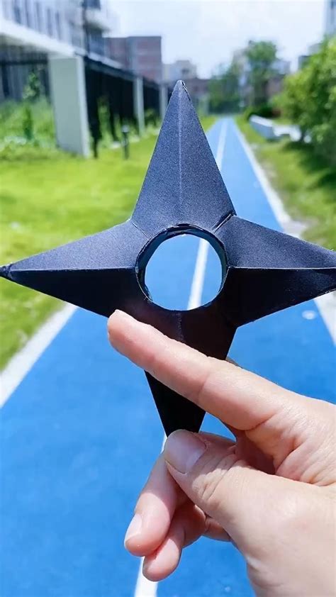Someone Holding Up A Black Origami Star On A Blue Track In The City