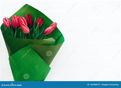 Beautiful Red Tulips Bouquet In Green Paper On White Wooden Background