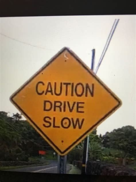 A Yellow Caution Drive Slow Sign Sitting On The Side Of A Road