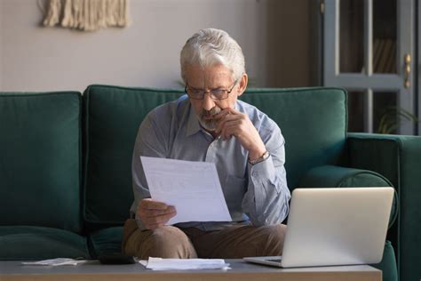 Serious Mature Man Sitting On Couch Received Invoice Analyzes Expenses
