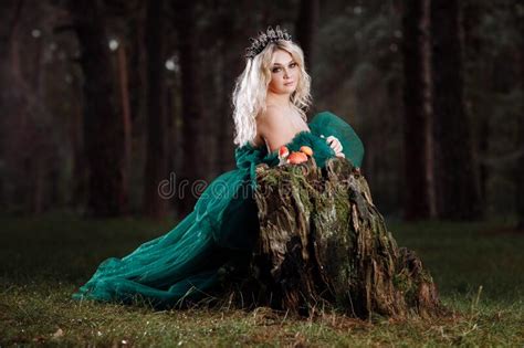 A Beautiful Blonde Young Woman In A Long Green Dress And A Diadem On Her Head In The Forest