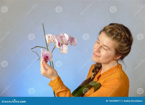 A Beautiful Girl With An Orchid In Her Hands Enjoys The Smell Of