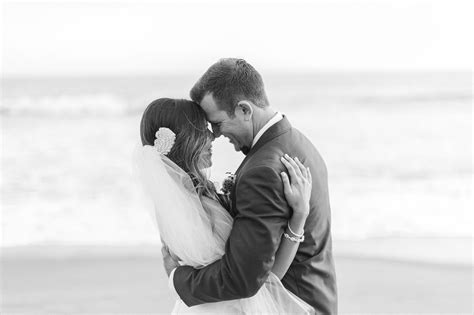 A Bride And Groom Embrace On The Beach In Front Of The Ocean While