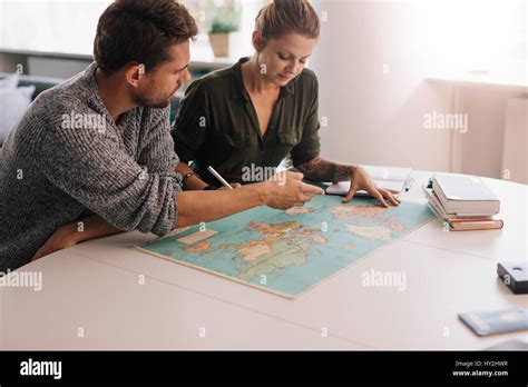 Man And Woman Discussing And Making Notes Pointing At The World Map