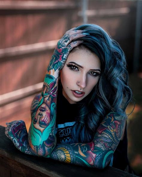 a woman with tattoos on her arms leaning against a wooden wall and looking at the camera