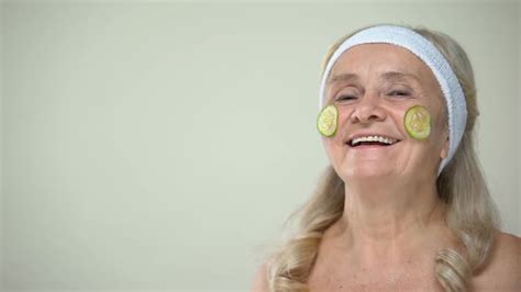 Funny Joyful Granny With Cucumber Mask On Face Biting One Slice And