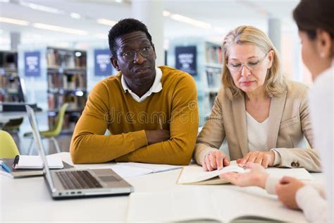 Female Tutor Helping Students Preparing For Exam In Library Stock Photo
