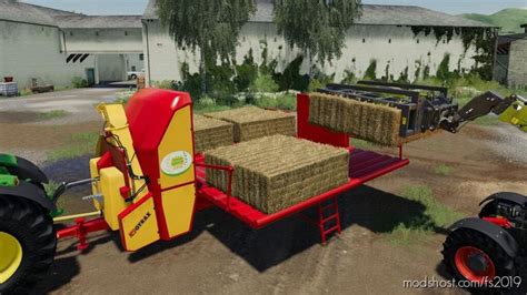 A Tractor Trailer With Hay Bales On The Back In Front Of A Farm Building