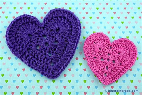 Two Crocheted Hearts Sitting Next To Each Other On A Blue And Pink Background
