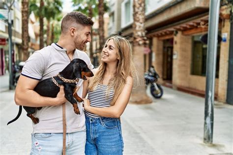 Young Caucasian Couple Hugging And Smiling Happy Standing With Dog At
