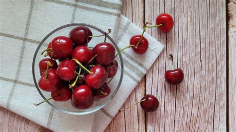 Sweet Red Cherries In Glass Bowl On Brown Wooden Old Table And White Napkin Next To The Bowl
