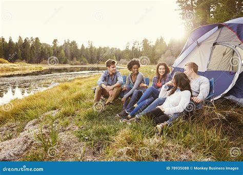 Friends On A Camping Trip Relaxing By Their Tent Near A Lake Stock