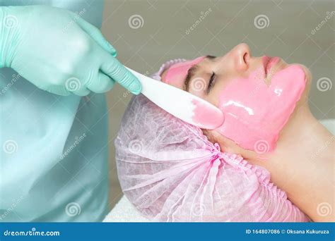 Face Of Young Woman Is Receiving Pink Facial Mask In Spa Salon Stock