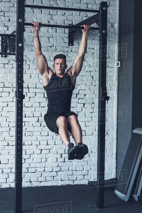 Young Man In Sportswear Doing Pull Ups On Pull Up Bar In Gym Stock