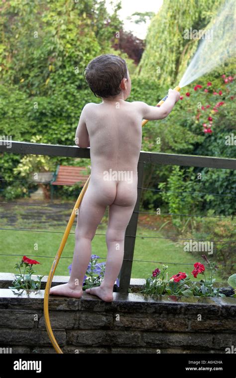 Joven niño nude desnuda desnuda en un jardín suburbano jugando con una
