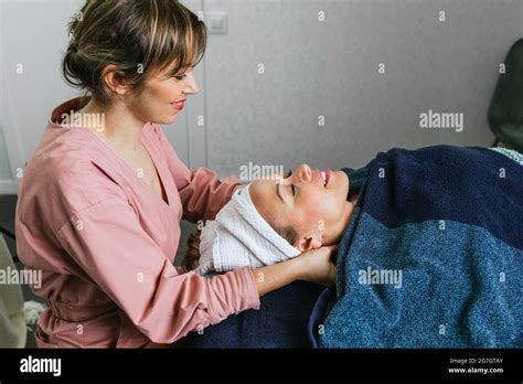 side view of content masseuse massaging shoulders of female client lying on table in beauty