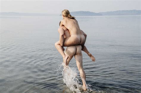 Nude Man Giving Nude Woman Piggyback Into Water Stock Photo