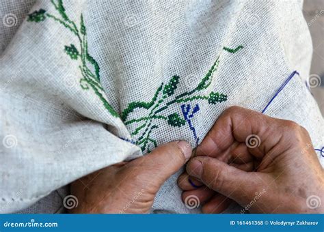 Hands Of An Elderly Woman Embroidering A Cross Stitch Floral Pattern On