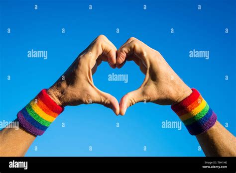 Gay Athlete Making Hand Heart With Gay Pride Rainbow Colors Wristbands Against Bright Blue Sky