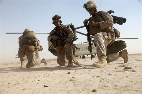 Three Soldiers Running Towards A Helicopter In The Desert