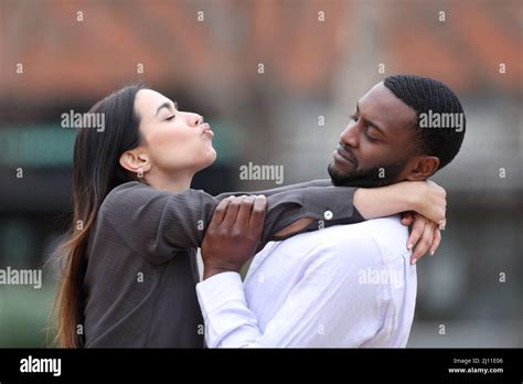Side View Portrait Of An Obsessed Woman Trying To Kiss A Man With Black Skin Who Rejects Her In