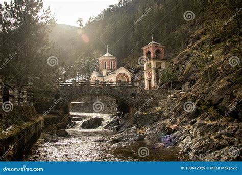 Small Church By The River And Stone Bridge On Fast River With Small