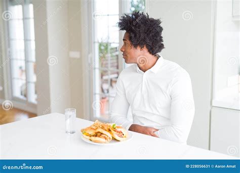 African American Hungry Man Eating Hamburger For Lunch Looking To Side Relax Profile Pose With
