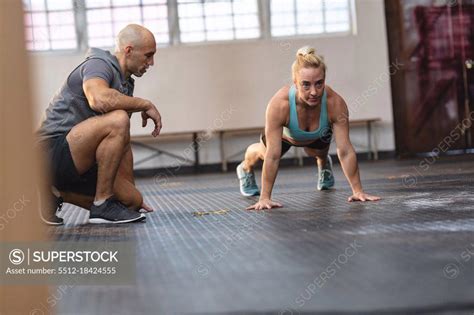 Caucasian Male Trainer Instructing Woman Exercising At Gym Doing Press
