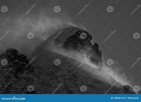 Grayscale Shot Of A Rocky Mountain Covered With Snow And Fog During