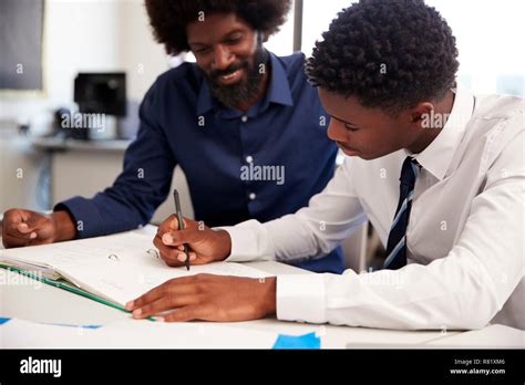 High School Tutor Giving Uniformed Male Student One To One Tuition At