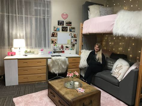 A Woman Sitting On A Couch In A Dorm Room With Her Bed And Dressers