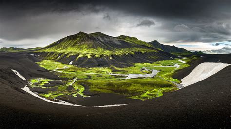 Landscape View Of Green And Black Covered Mountain In Iceland Under Black And White Cloudy Sky